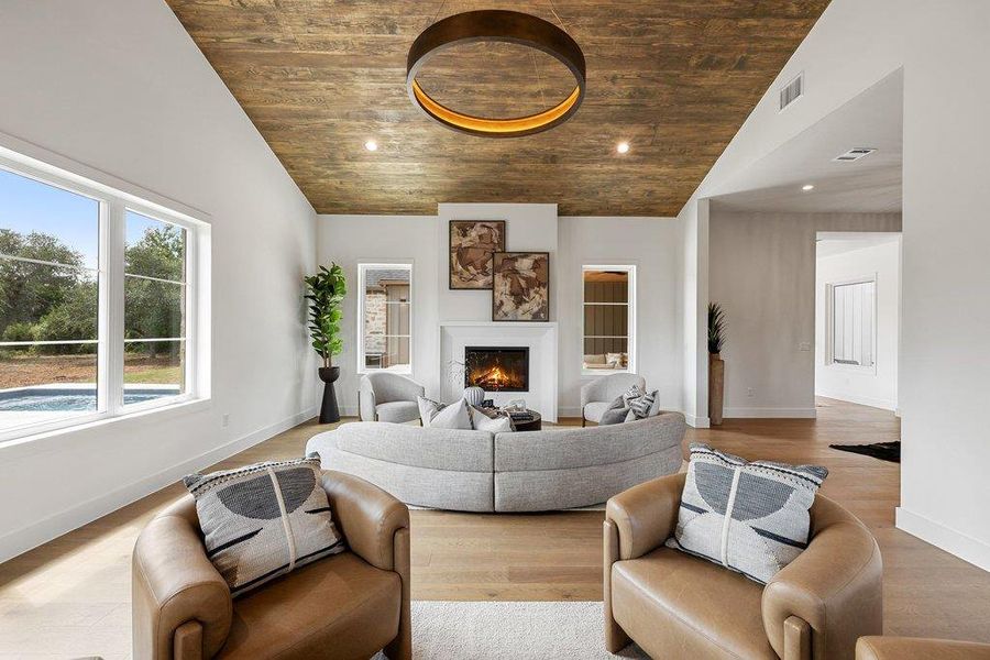 An inviting living room features a striking wood-paneled ceiling, a cozy fireplace, and direct views of a private pool.