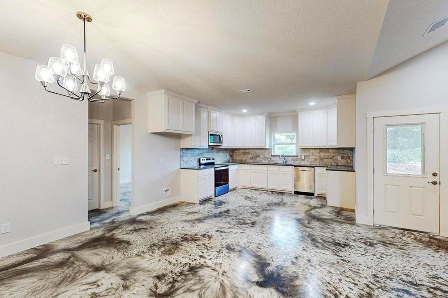 Kitchen featuring white cabinets, hanging light fixtures, decorative backsplash, a notable chandelier, and stainless steel appliances