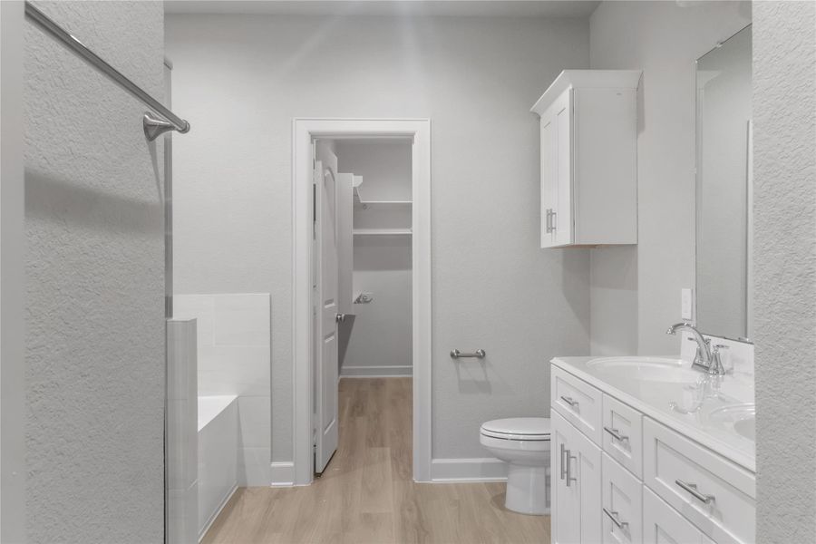 This photo showcases a modern bathroom with a dual-sink vanity, sleek white cabinetry, and a built-in bathtub. The space features light wood flooring and neutral wall tones, creating a clean and bright atmosphere.