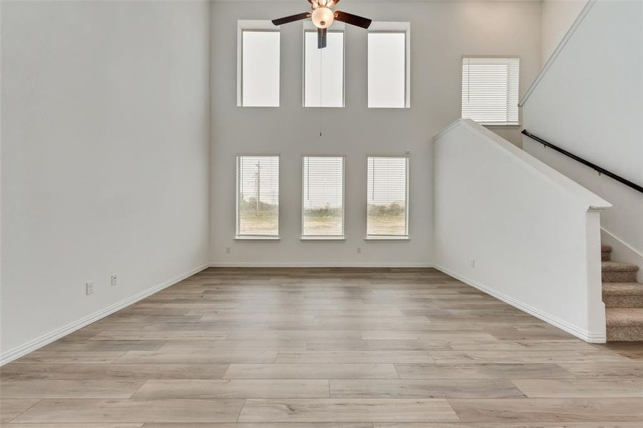 Unfurnished living room featuring light hardwood / wood-style flooring, a high ceiling, and ceiling fan