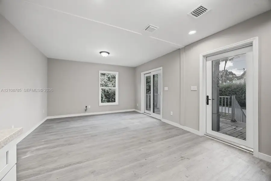 Neutral interior featuring wood-finish flooring, recessed lighting, double glass sliding doors, and a window with exterior greenery Neutral interior featuring wood-finish flooring, recessed lighting, double glass sliding doors, and a window with exterior greenery