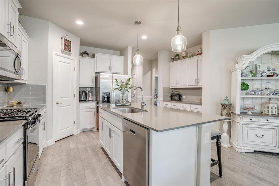 Kitchen with stainless steel appliances, backsplash, light wood-type flooring, and a sink