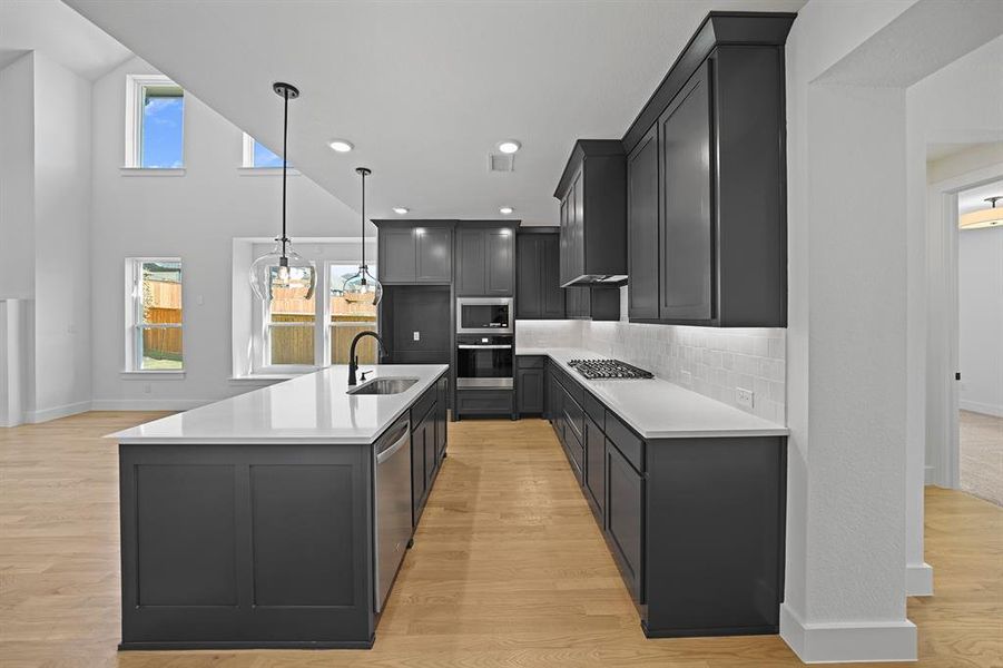 Kitchen featuring tasteful backsplash, light wood-style floors, hanging light fixtures, dark cabinets, and recessed lighting Kitchen featuring tasteful backsplash, light wood-style floors, hanging light fixtures, dark cabinets, and recessed lighting