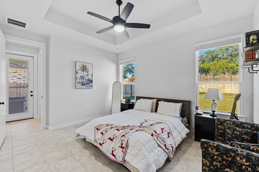 Bedroom featuring a tray ceiling, a ceiling fan, light tile patterned flooring, and multiple windows