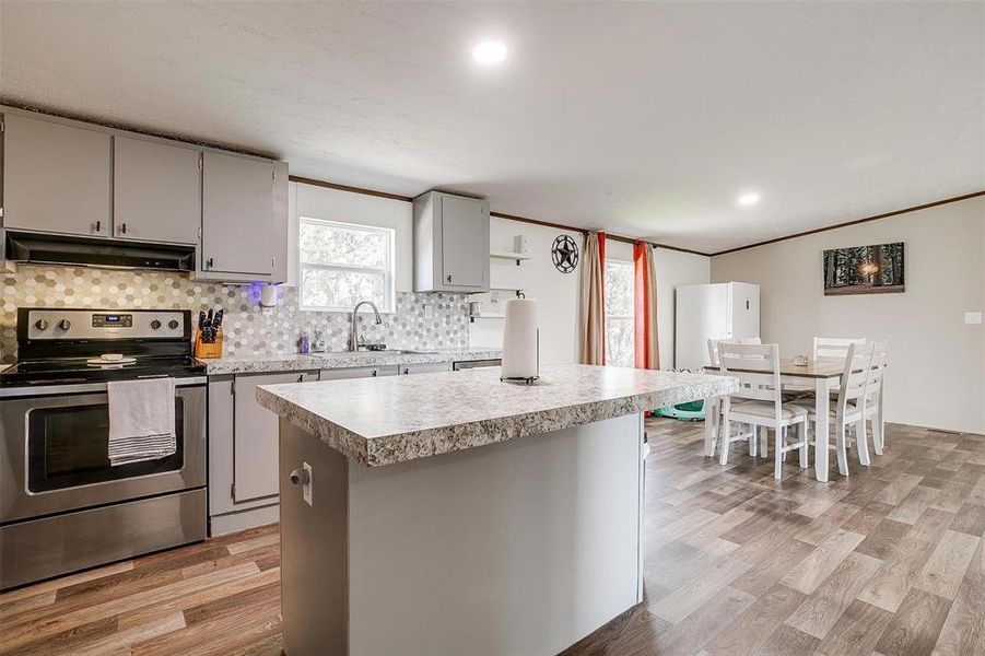 Kitchen featuring stainless steel electric range, sink, light hardwood / wood-style floors, and a kitchen island