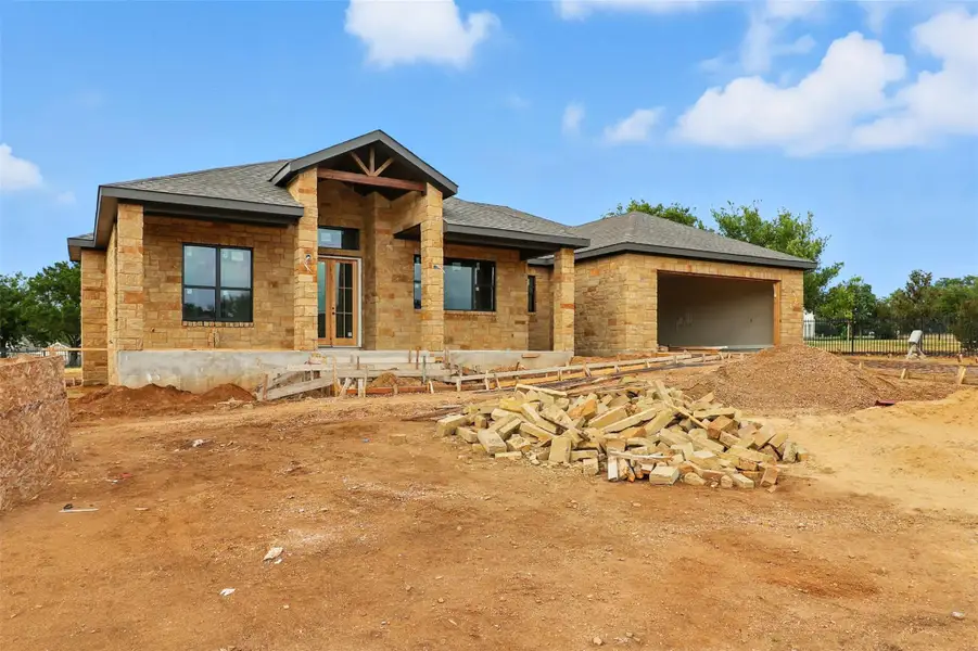 View of front facade with stone siding, a garage, a shingled roof, and a patio area View of front facade with stone siding, a garage, a shingled roof, and a patio area