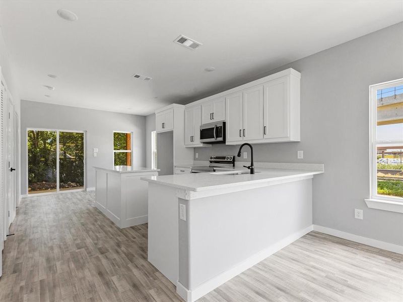 Kitchen featuring stainless steel appliances, light wood-style flooring, light countertops, baseboards, and white cabinets