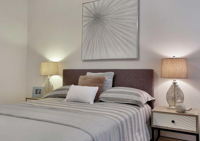 Bed with gray linens, side tables with lamps and a decorative wall hanging. Bed with gray linens, side tables with lamps and a decorative wall hanging.
