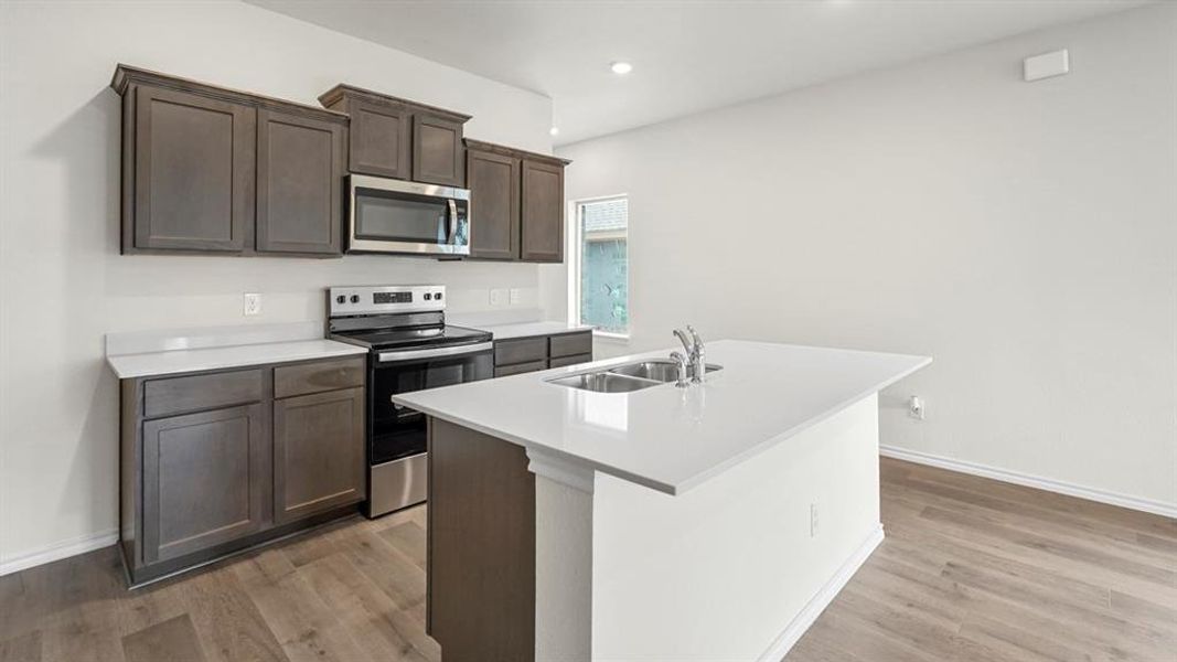 Modern kitchen featuring an island with a double sink, stainless steel appliances, dark wood-finish cabinetry, light countertops, and wood-finish flooring