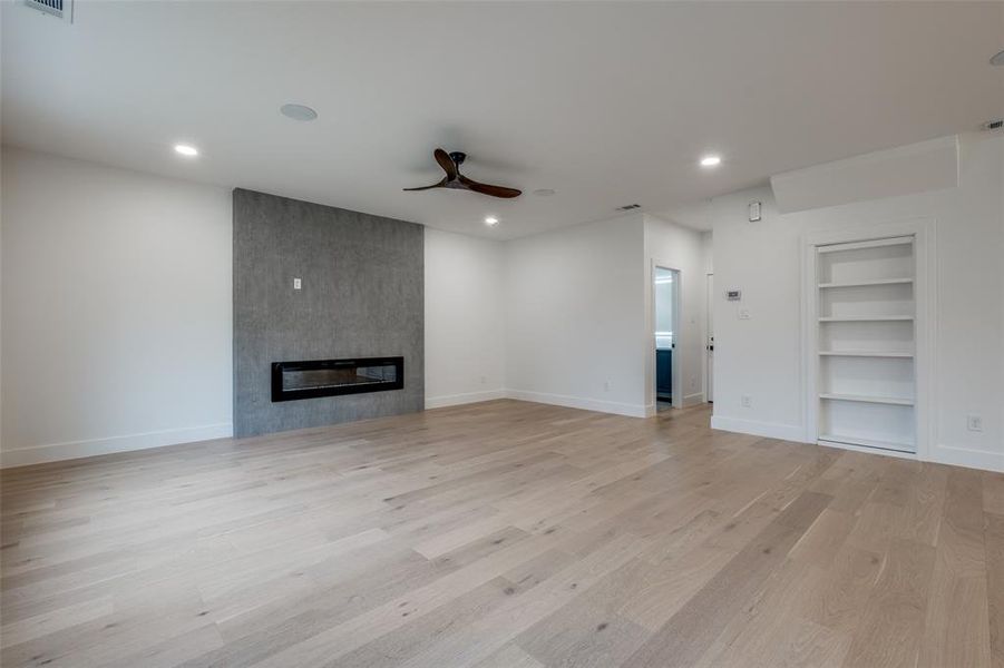 Living room with built in shelves, light wood-style floors, ceiling fan, recessed lighting, and a large fireplace