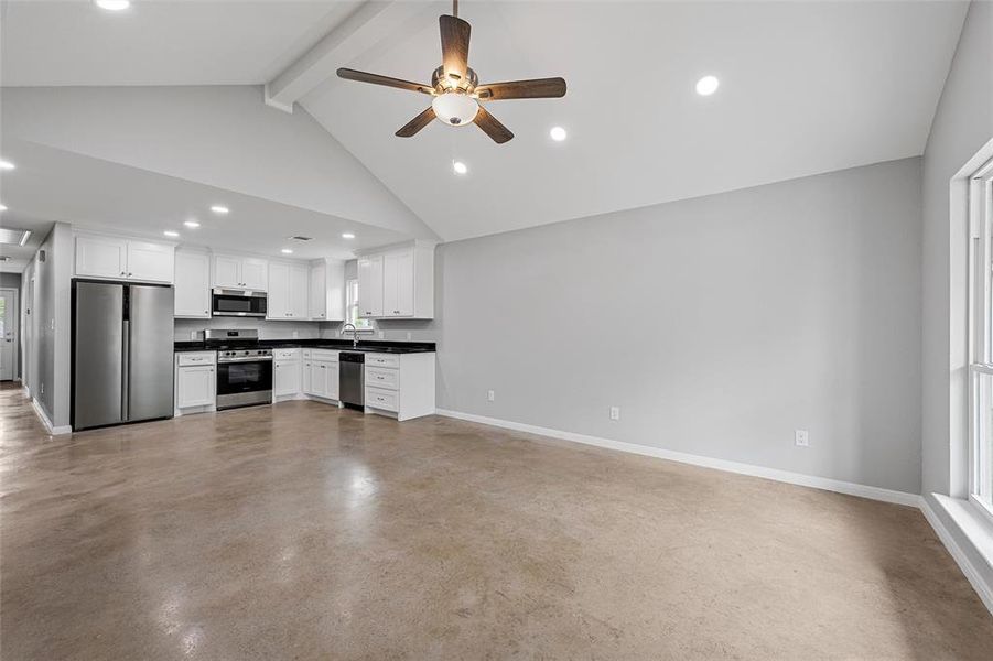 Unfurnished living room with beamed ceiling, a sink, concrete flooring, a ceiling fan, and baseboards