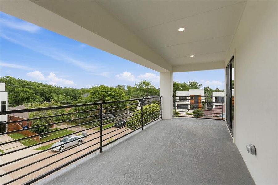 Expansive outdoor balcony featuring a concrete surface, black metal railings, recessed lighting, and a white stucco exterior Expansive outdoor balcony featuring a concrete surface, black metal railings, recessed lighting, and a white stucco exterior