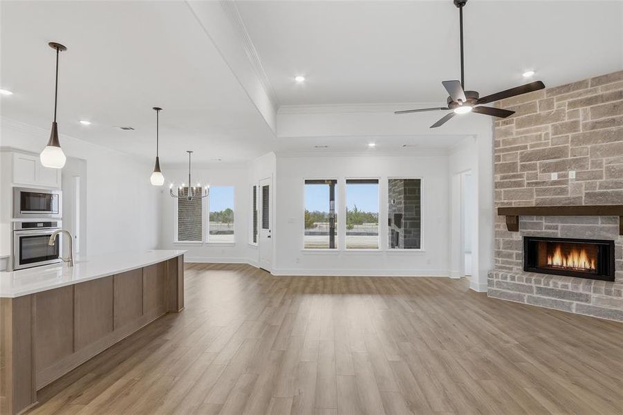 Unfurnished living room with a fireplace, light wood finished floors, a ceiling fan, ornamental molding, and suspended lighting