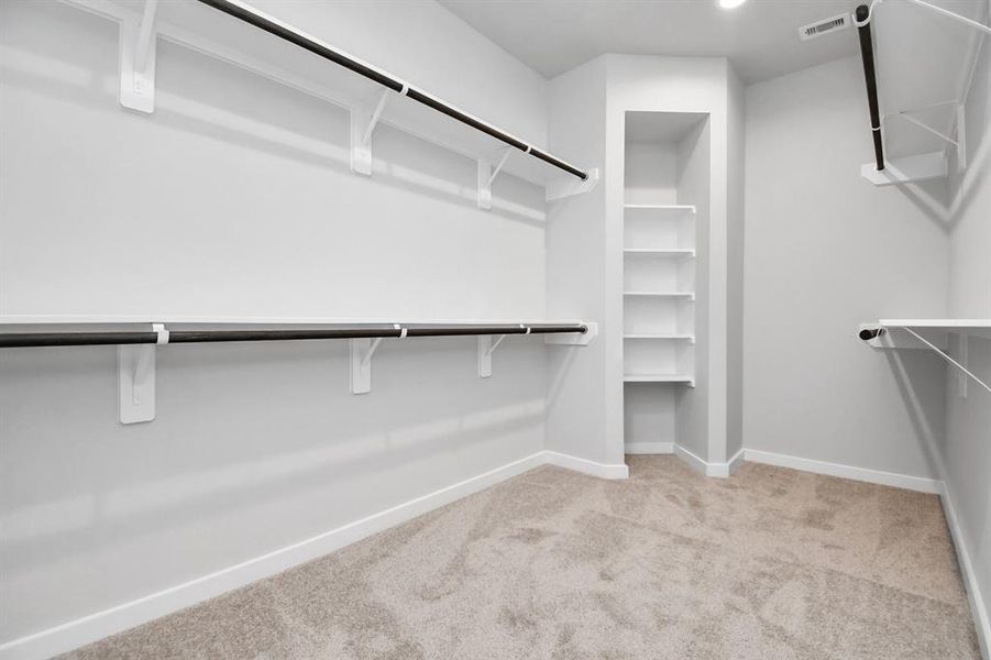 Spacious walk-in closet with high ceilings and plush carpet. Warm paint tones, built-in shelving, and dark finishes create a contemporary and functional retreat. Sample photo of completed home with similar floor plan. As-built interior colors and selections may vary.