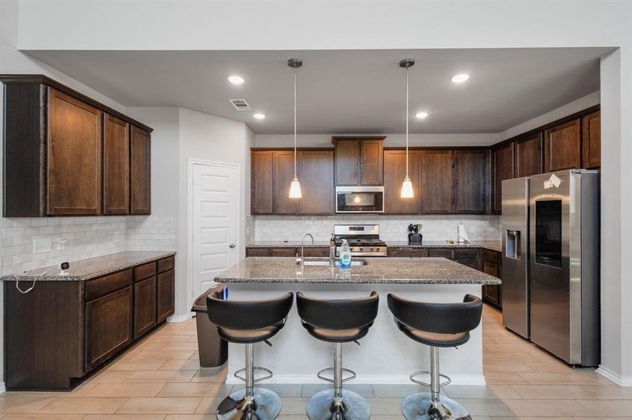 Kitchen with stainless steel appliances, a kitchen bar, decorative light fixtures, light stone countertops, and backsplash Kitchen with stainless steel appliances, a kitchen bar, decorative light fixtures, light stone countertops, and backsplash
