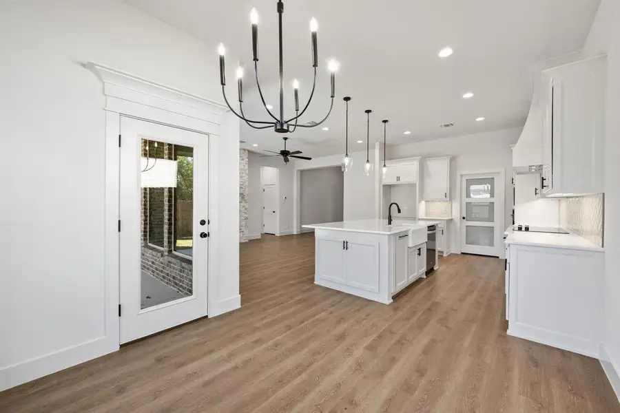Kitchen featuring an island with sink, white cabinetry, open floor plan, a chandelier, and ceiling fan