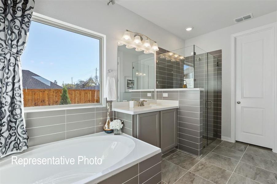 Soaking tub with a large window, glass-enclosed shower, single vanity with a white countertop, and tiled flooring