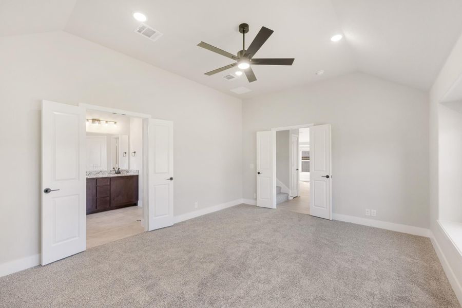 Empty master bedroom with carpet, ceiling fan, and open doors to ensuite bathroom and hallway