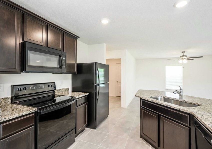 Caladesi floor plans kitchen with recessed lighting, tile floors, black kitchen appliances and dark brown cabinets.