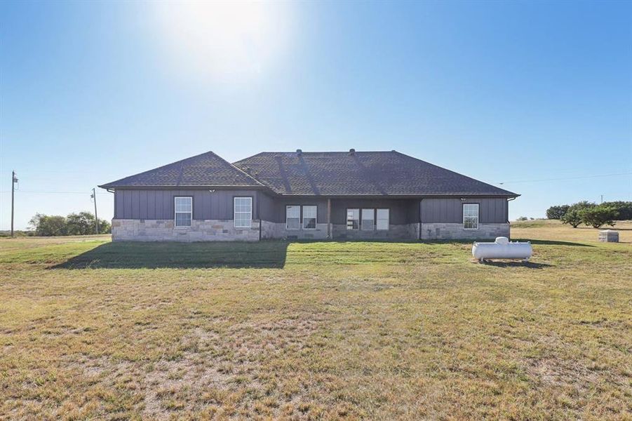 Rear view of property with board and batten siding, stone siding, and a yard