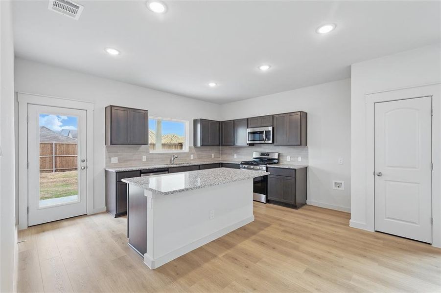 Kitchen featuring stainless steel appliances, a center island, light wood-type flooring, dark wood finish cabinets, and tasteful backsplash