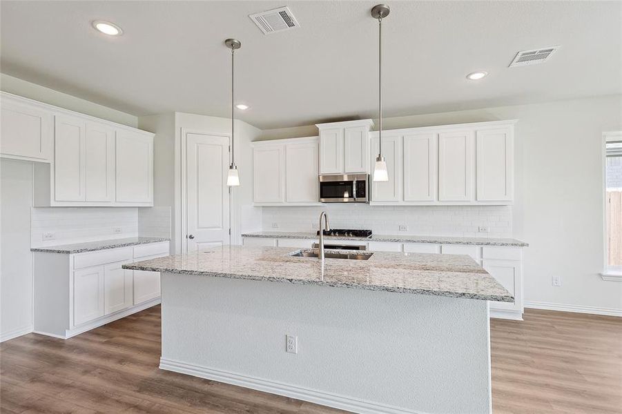 Kitchen with white cabinets, wood-type flooring, and an island with sink