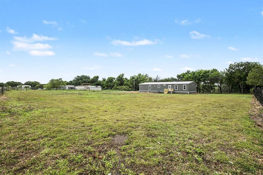 Expansive green space featuring a single-story residence with a gray exterior siding and white trim windows
