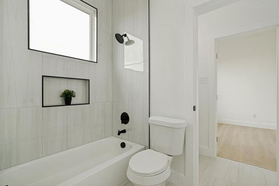 Bathroom featuring a white soaking tub, matte black fixtures, a tiled shower surround, a built-in shower niche, and a contemporary window Bathroom featuring a white soaking tub, matte black fixtures, a tiled shower surround, a built-in shower niche, and a contemporary window