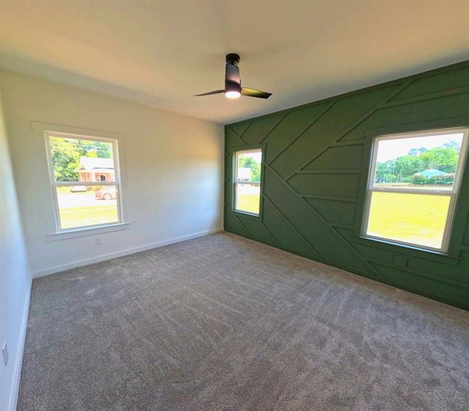 Carpeted spare room featuring a decorative wall and a ceiling fan Carpeted spare room featuring a decorative wall and a ceiling fan