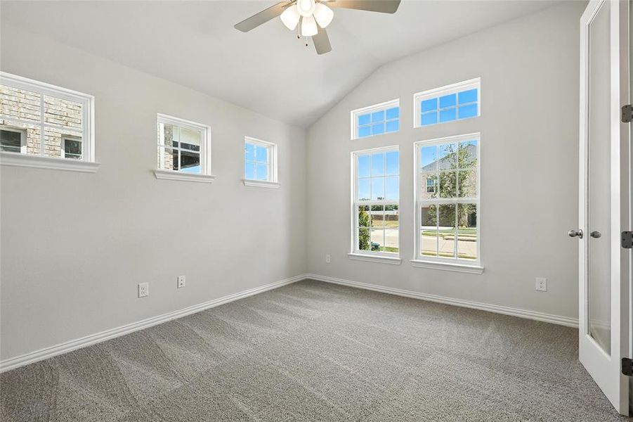 Empty room featuring a ceiling fan, lofted ceiling, carpet flooring, and plenty of natural light Empty room featuring a ceiling fan, lofted ceiling, carpet flooring, and plenty of natural light