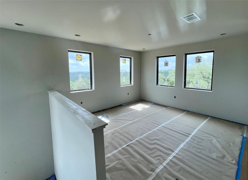This room features four windows providing views of the surrounding trees and hills, recessed lighting, and an overhead ventilation system