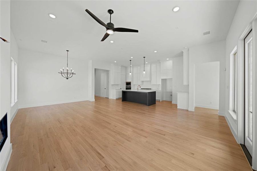 Unfurnished living room featuring recessed lighting, light wood-style floors, ceiling fan, and a chandelier Unfurnished living room featuring recessed lighting, light wood-style floors, ceiling fan, and a chandelier