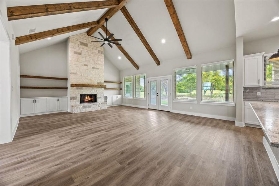 Unfurnished living room with light wood finished floors, high vaulted ceiling, a stone fireplace, beam ceiling, and french doors Unfurnished living room with light wood finished floors, high vaulted ceiling, a stone fireplace, beam ceiling, and french doors