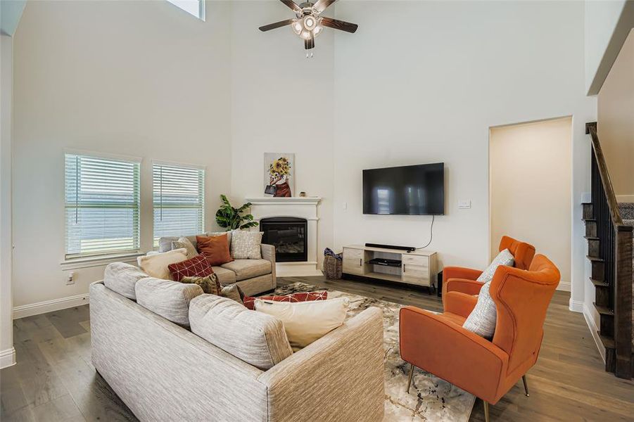 Living area featuring a glass covered fireplace, wood finished floors, a high ceiling, and ceiling fan