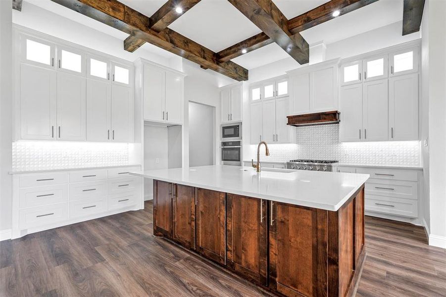 Kitchen featuring black microwave, an island with sink, beam ceiling, oven, and tasteful backsplash