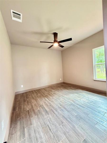 Spacious room featuring wood-finish tile flooring, neutral wall tones, and an overhead ceiling fan with integrated lighting Spacious room featuring wood-finish tile flooring, neutral wall tones, and an overhead ceiling fan with integrated lighting