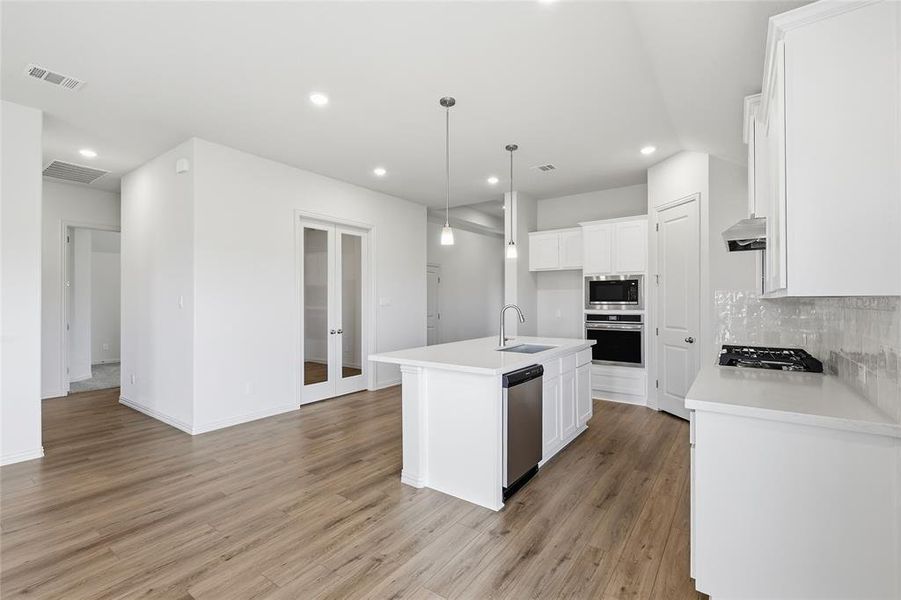 Kitchen featuring white cabinets, stainless steel appliances, a center island with sink, and tasteful backsplash