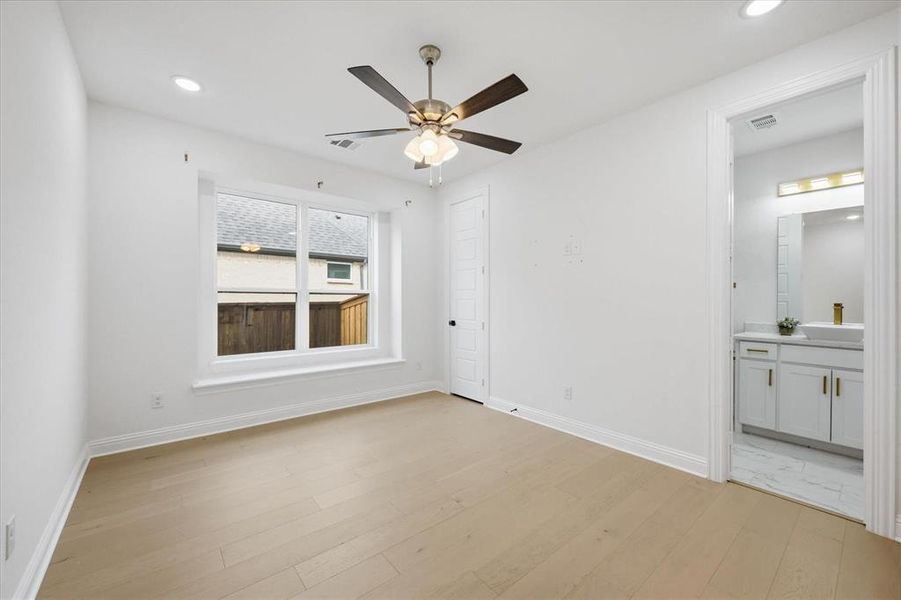 Bright room featuring a large window, light wood-finish flooring, recessed lighting, a ceiling fan, and direct access to a full bathroom