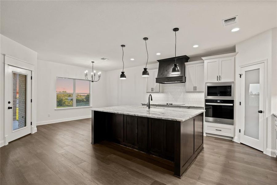 Kitchen with appliances with stainless steel finishes, tasteful backsplash, white cabinetry, decorative light fixtures, and premium range hood
