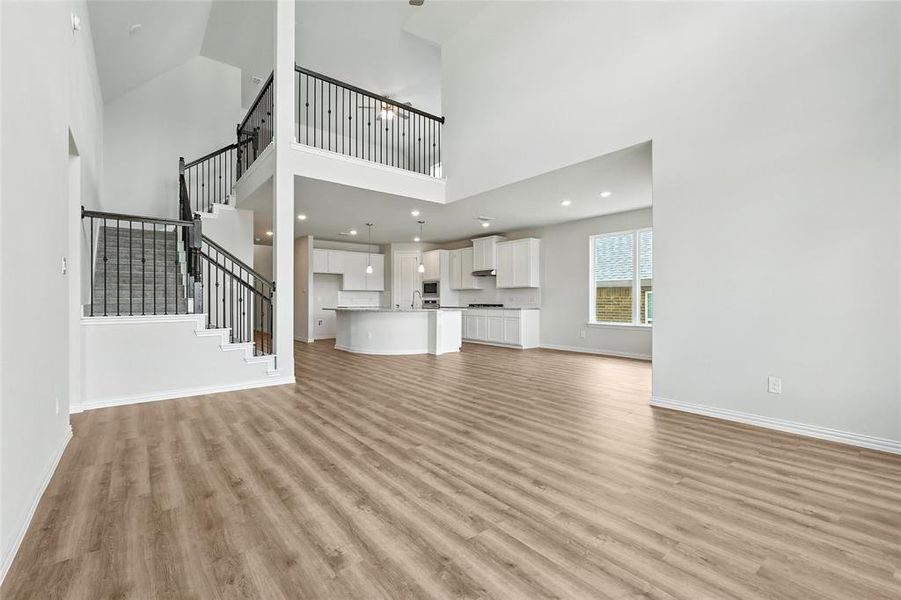Unfurnished living room featuring light wood finished floors, a towering ceiling, stairs, and recessed lighting Unfurnished living room featuring light wood finished floors, a towering ceiling, stairs, and recessed lighting