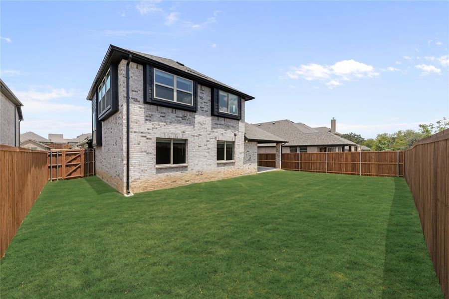 Two-story brick home with black trim windows, large grassy backyard, and wood privacy fence