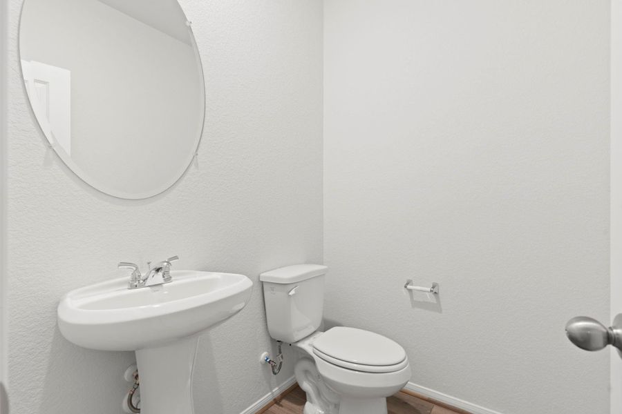 The half bath is conveniently located on the main level, offering modern fixtures, a round mirror, and a clean, fresh design that adds both style and practicality for guests and family alike.