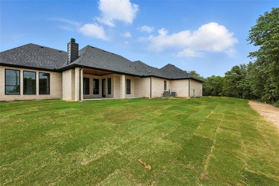Rear view of property with brick siding, roof with shingles, and a yard