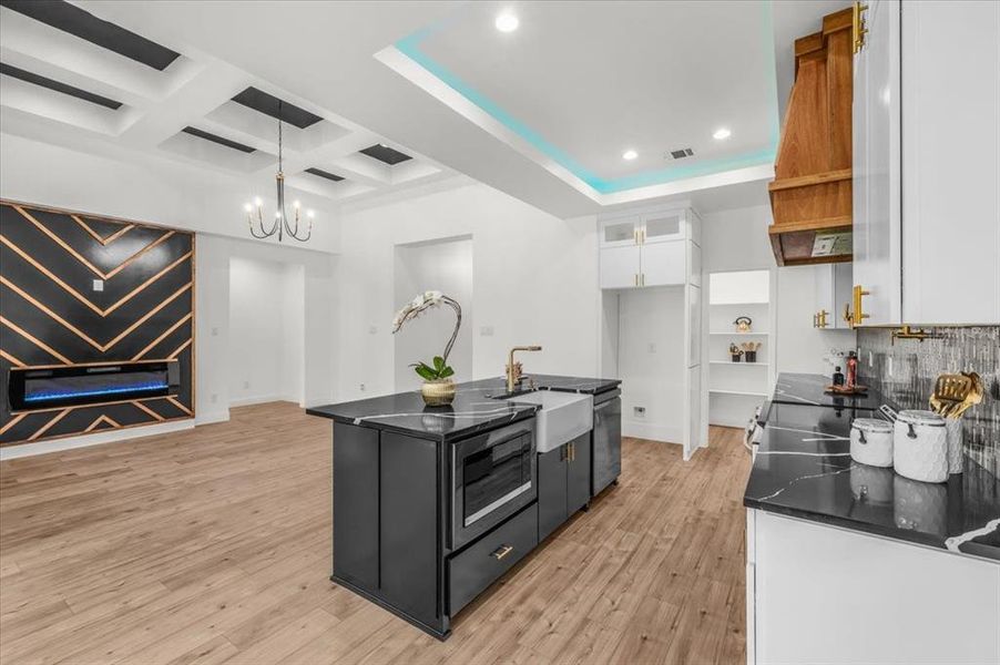 Kitchen with white cabinets, a center island with sink, pendant lighting, backsplash, and light wood-style floors