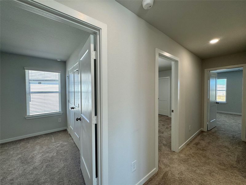 Bright, carpeted upstairs hallway leading to three bedrooms and a full bathroom, featuring white walls, doors, and ample natural light. Bright, carpeted upstairs hallway leading to three bedrooms and a full bathroom, featuring white walls, doors, and ample natural light.