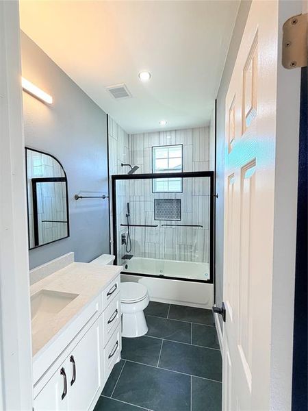 Bathroom featuring a white vanity with integrated sink, a tiled tub/shower combination with a glass enclosure, dark gray floor tile, and recessed lighting