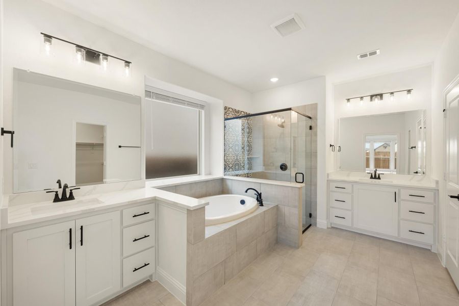 Master bathroom with dual vanities, soaking tub, glass walk-in shower, and white cabinets with black hardware