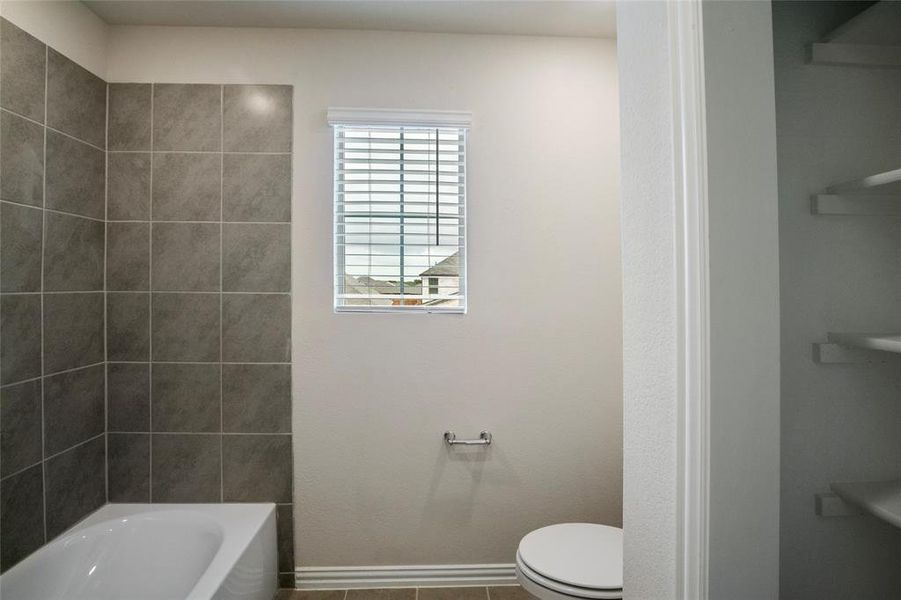 Bathroom featuring tile patterned flooring, tiled shower / bath combo, and toilet