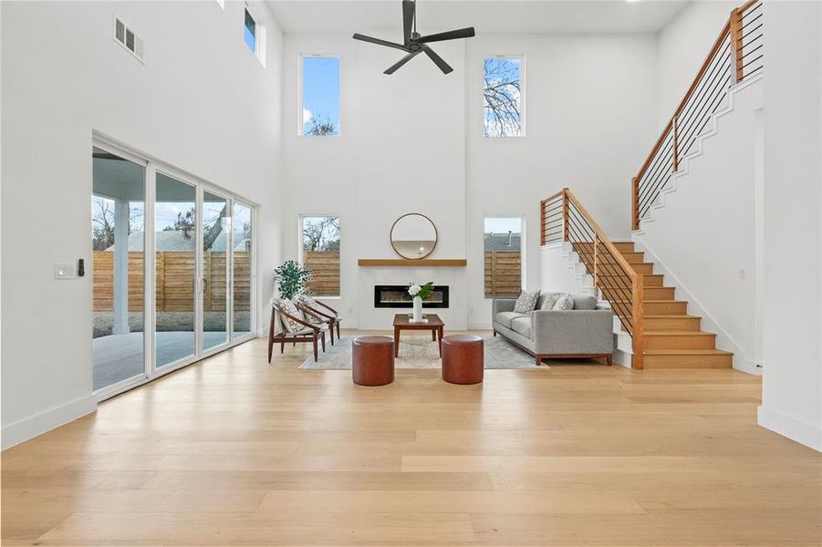 Living area with a fireplace, light wood finished floors, a ceiling fan, and a high ceiling