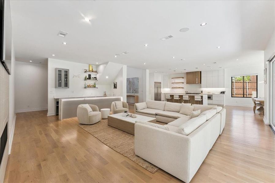Living room with light wood-style floors, bar, and recessed lighting